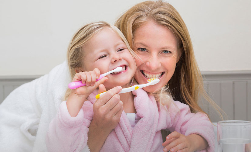 A mother showing her daughter how to brush her teeth.