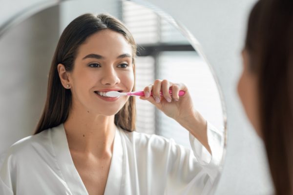 woman brushing her teeth in mirror